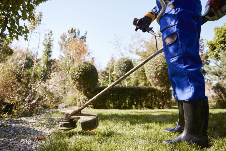 jardinero-con-weedwacker-cortando-el-cesped-en-el-jardin-scaled